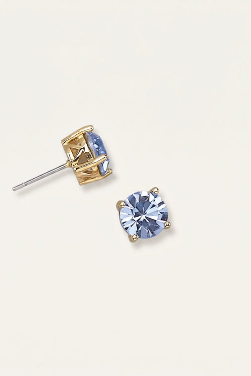 A pair of gold stud earrings with oval light blue gemstones, one shown from the front and the other from the side/back, on a light cream background.