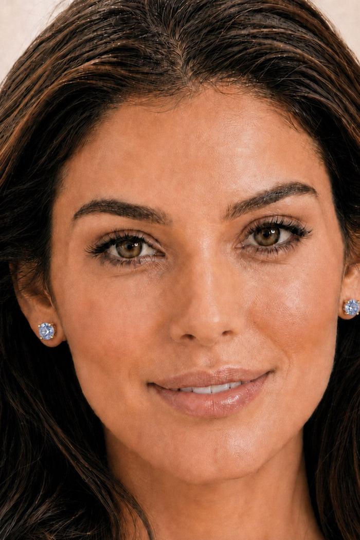Close-up portrait of a woman wearing small round stud earrings with clear gemstones in silver-toned settings.
