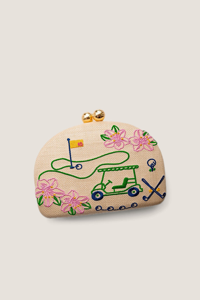 A small beige fabric coin purse with gold-tone clasp hardware, decorated with embroidered golf-themed motifs including a green golf cart, pink flowers, a flagstick, and crossed clubs on a white background.
