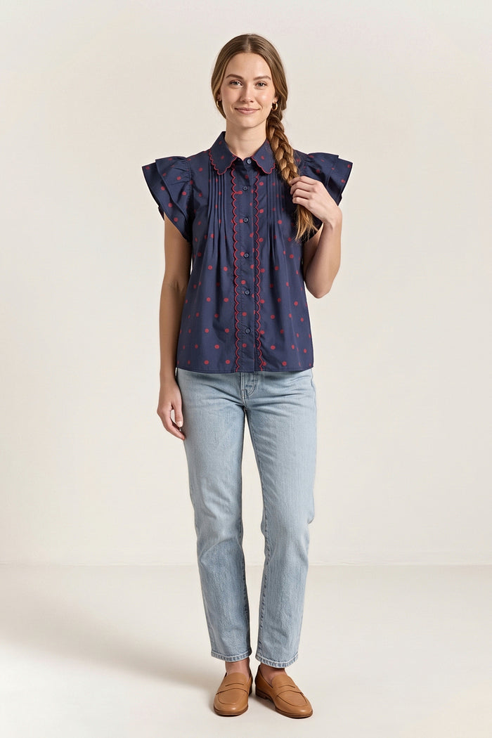 Front view of the navy blouse with small red dots, a red scalloped collar and placket trim and flutter sleeves.