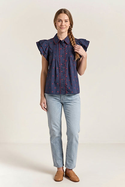 Front view of the navy blouse with small red dots, a red scalloped collar and placket trim and flutter sleeves.